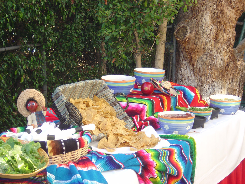 Large catering table with bright multicolor table clothes and bowls and figurine with a hat and chips spilling from a basket