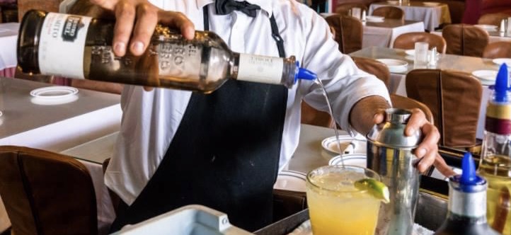 A person pouring tequila into a margarita with assorted bottles around him.