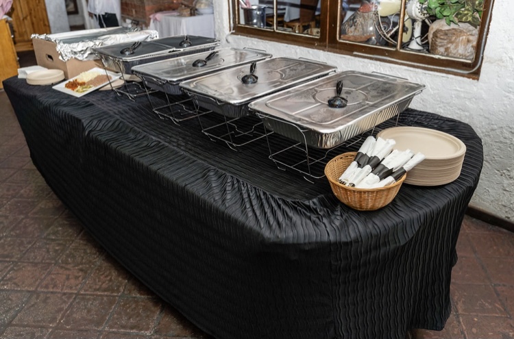 Catering table with wire chafing dishes covered with lids, napkins and plates