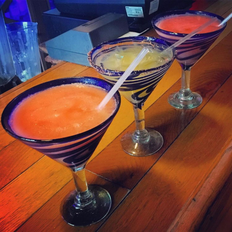 three margaritas of different flavors with straws on a bar